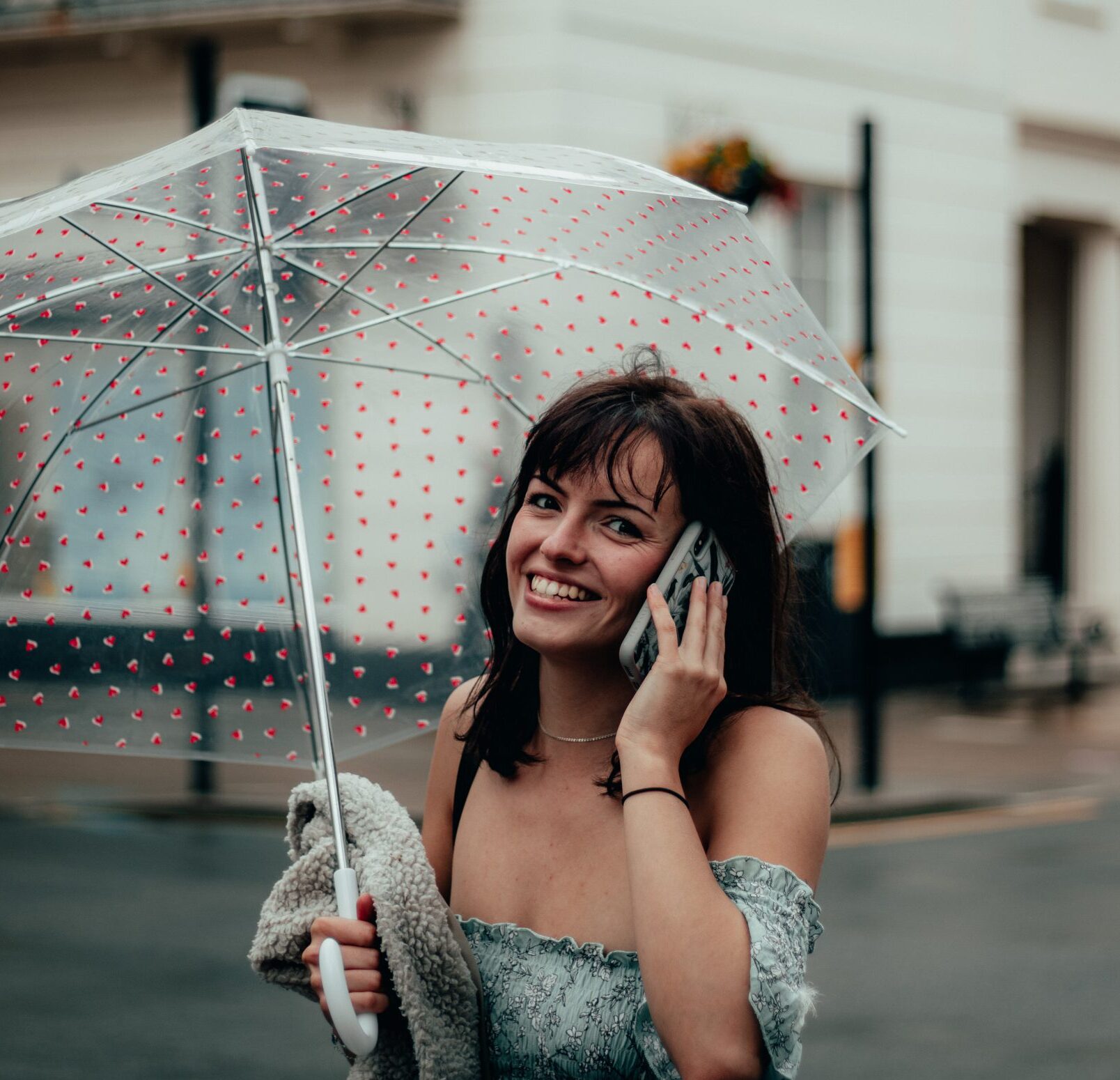 young girl on the phone sheltering under an umbrella from the rain